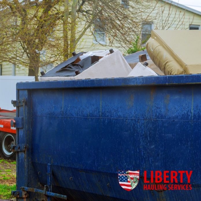 A large blue roll-off dumpster placed on a construction site, surrounded by debris and construction materials, with a clear sky in the background.